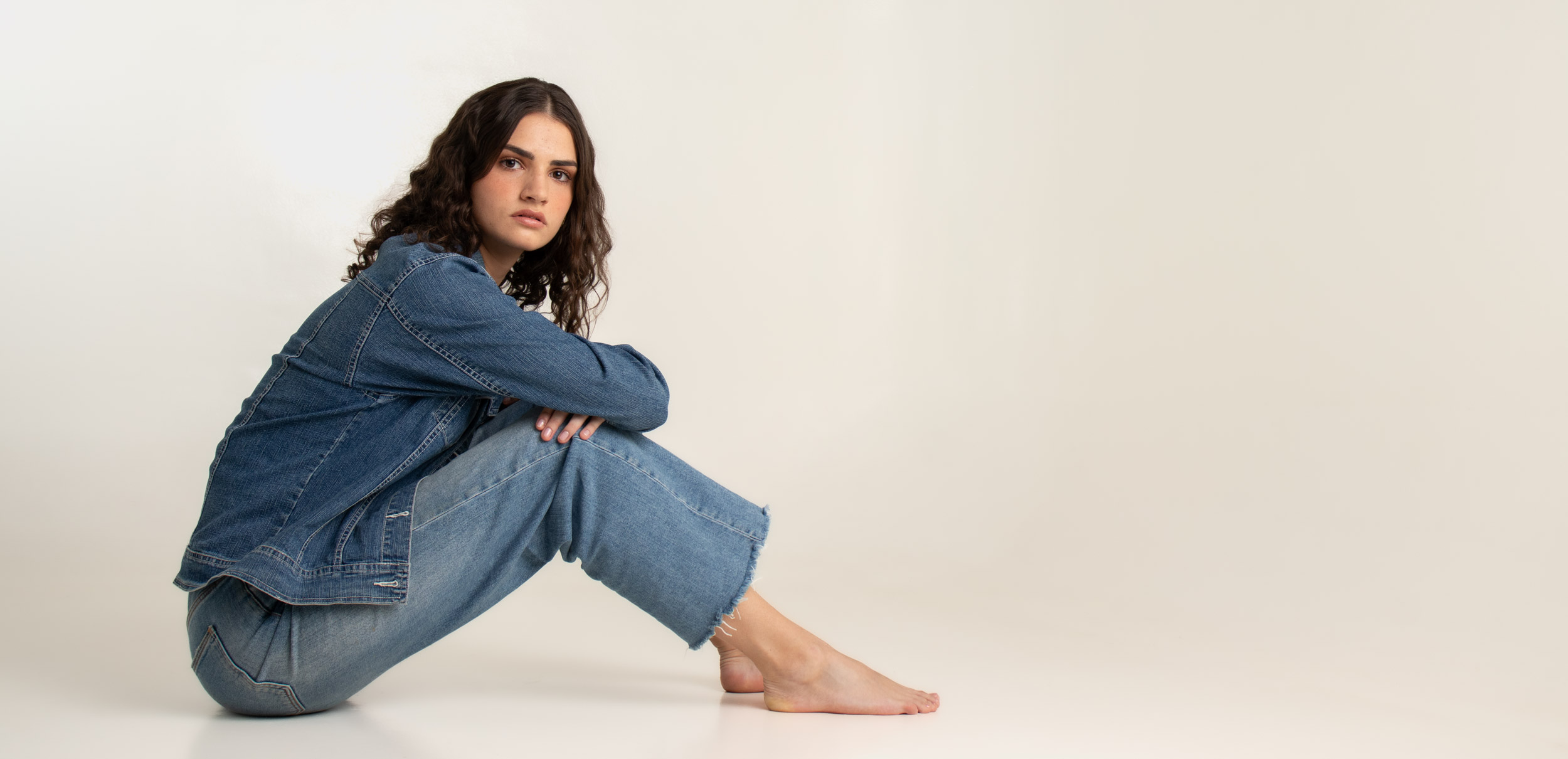 A brunette girl wearing denims on a white studio curve